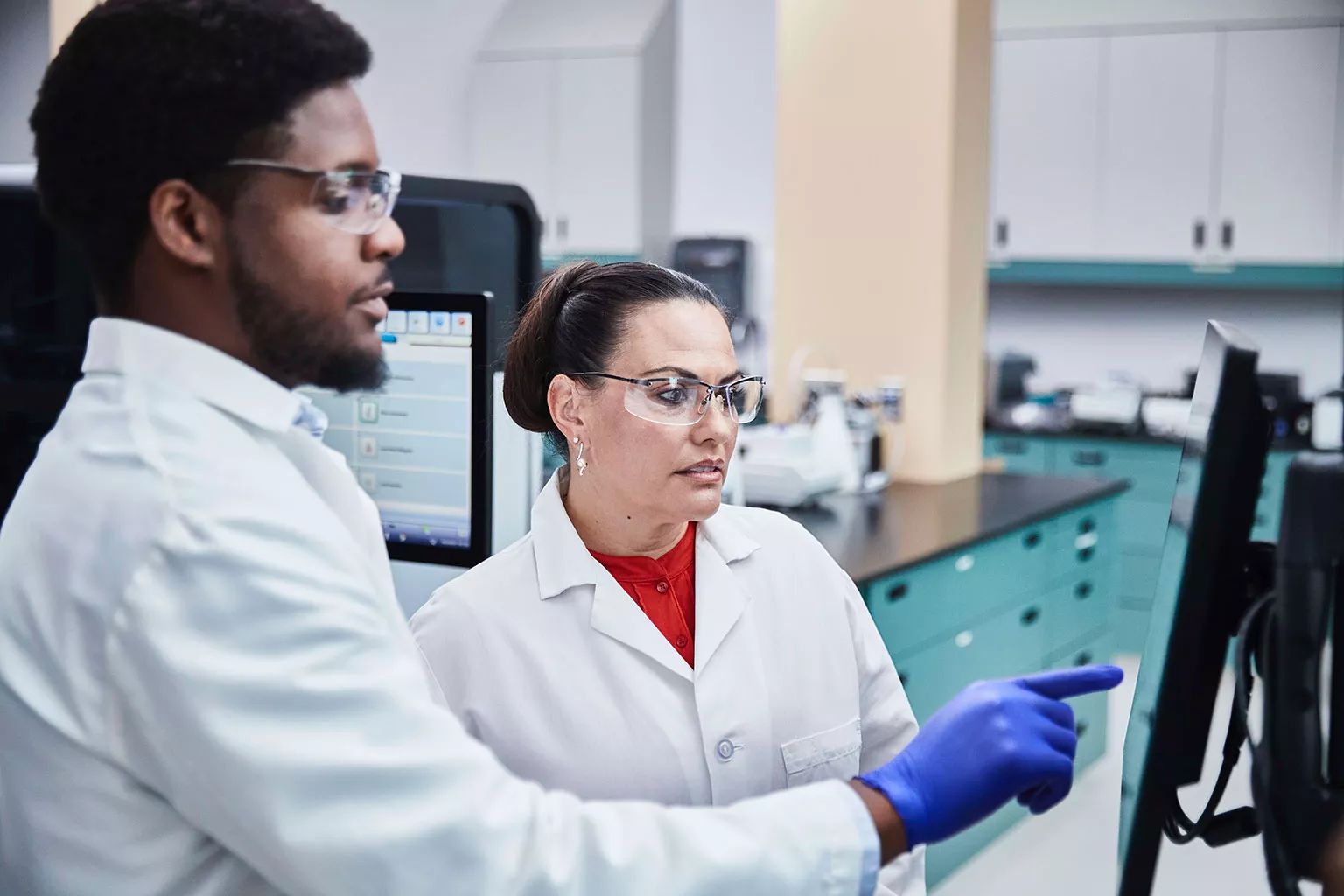 Auf einen Bildschirm blickender und zeigender Labortechniker in Laborumgebung